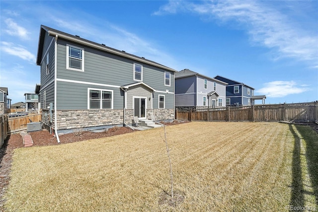 rear view of property with stone siding, a lawn, a fenced backyard, and entry steps