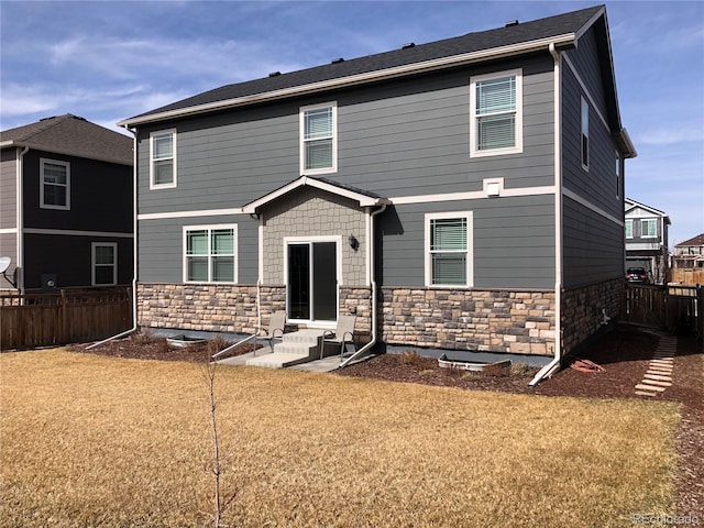 rear view of house featuring a yard, stone siding, fence, and entry steps