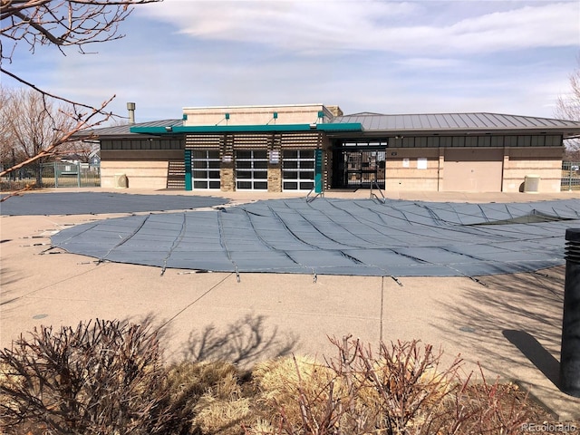 exterior space featuring a standing seam roof, a community pool, fence, and metal roof