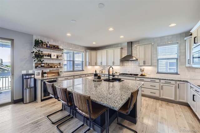 16345 Spanish Peak Way, Broomfield, CO 80023 - kitchen featuring wall chimney exhaust hood, a sink, wine cooler, light wood finished floors, and a kitchen island with sink