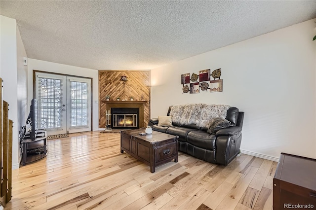 living area with french doors, wood walls, light wood finished floors, a textured ceiling, and a glass covered fireplace