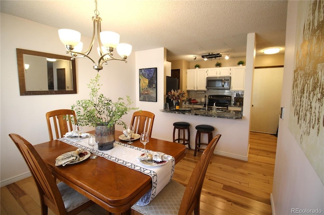 dining space featuring light wood-style floors, baseboards, a textured ceiling, and an inviting chandelier