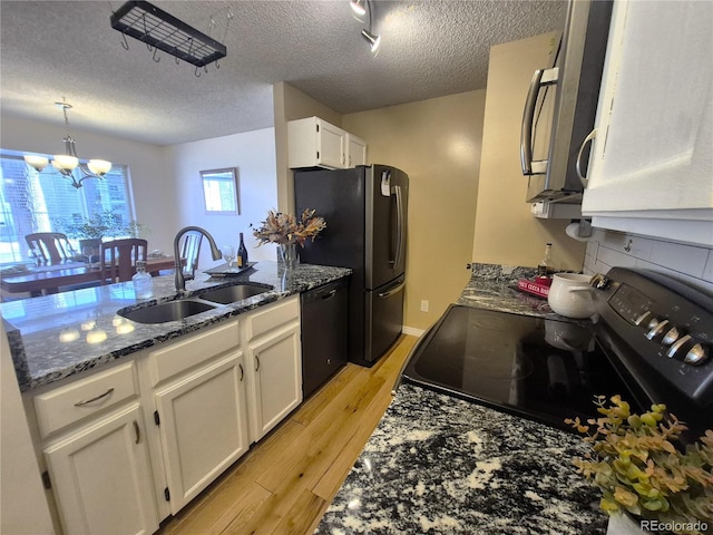 kitchen with white cabinets, light wood-style floors, dark stone countertops, black appliances, and a sink