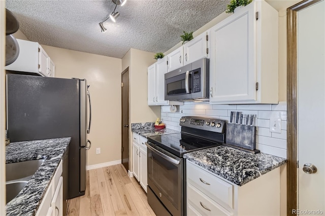 kitchen featuring light wood finished floors, decorative backsplash, stainless steel appliances, white cabinetry, and a sink