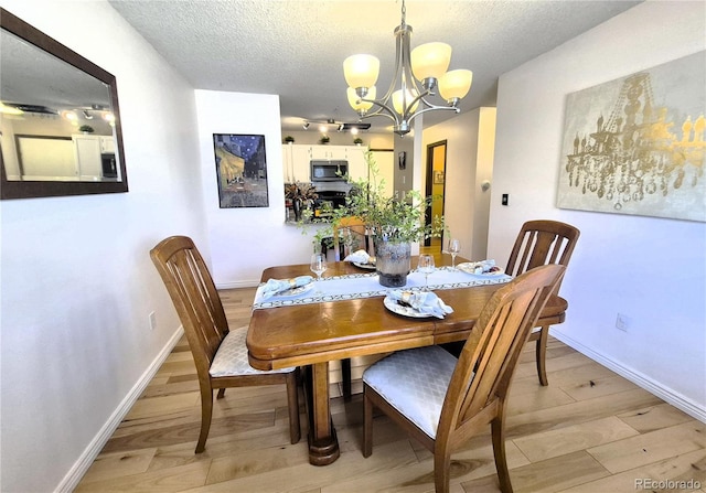 dining space with an inviting chandelier, light wood-style flooring, baseboards, and a textured ceiling