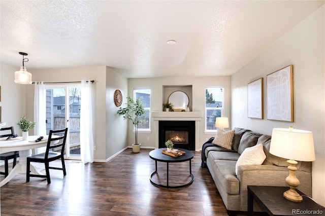 living room with a warm lit fireplace, dark wood-style flooring, a textured ceiling, and baseboards