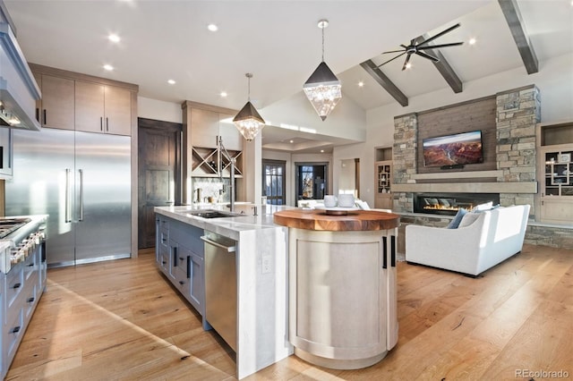 3947 Taliesin Way, Fort Collins, CO 80524 - kitchen featuring light wood finished floors, a center island with sink, a stone fireplace, appliances with stainless steel finishes, and exhaust hood