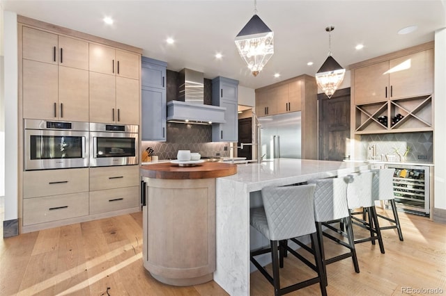 3947 Taliesin Way, Fort Collins, CO 80524 - kitchen with light wood finished floors, wine cooler, a large island with sink, stainless steel appliances, and wall chimney exhaust hood