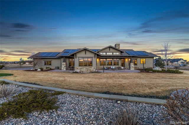 3947 Taliesin Way, Fort Collins, CO 80524 - back of house at dusk with roof mounted solar panels, a lawn, a chimney, and a patio