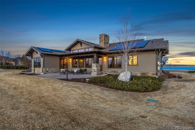 3947 Taliesin Way, Fort Collins, CO 80524 - back of property featuring solar panels, a shingled roof, a chimney, stone siding, and a patio area