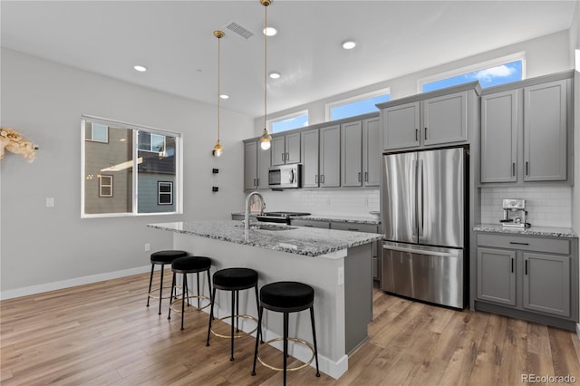 kitchen featuring appliances with stainless steel finishes, a kitchen bar, gray cabinetry, and a sink