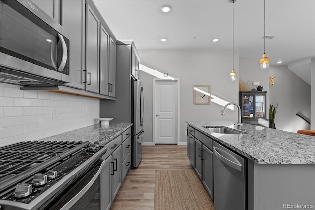 kitchen with hanging light fixtures, a kitchen island with sink, gray cabinets, appliances with stainless steel finishes, and sink