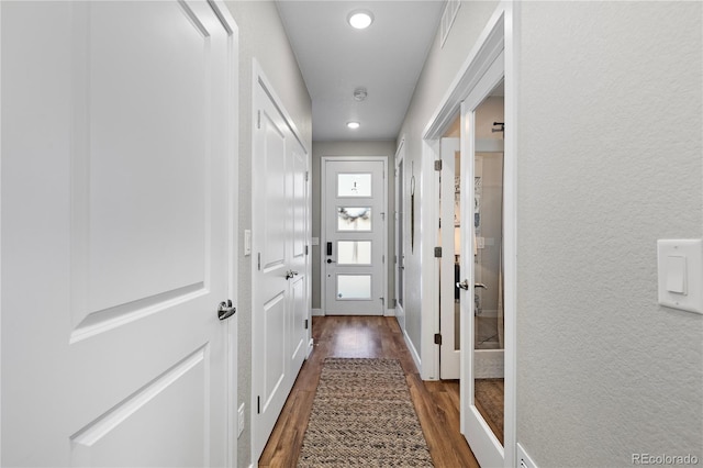 doorway featuring dark wood finished floors, recessed lighting, a textured wall, and baseboards