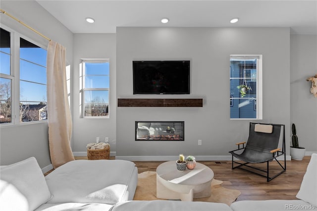 living area with a glass covered fireplace, wood finished floors, and baseboards