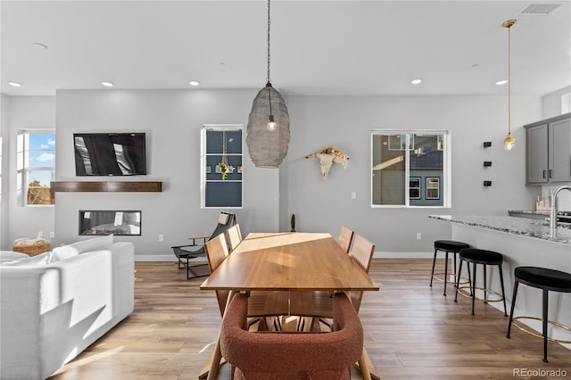 dining area with a glass covered fireplace, recessed lighting, light wood-type flooring, and baseboards