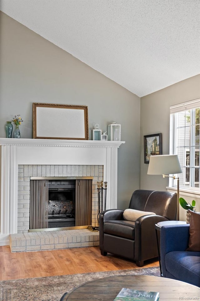 8997 W 88th Ave, Westminster, CO 80021 - living area with lofted ceiling, wood finished floors, a brick fireplace, and a textured ceiling