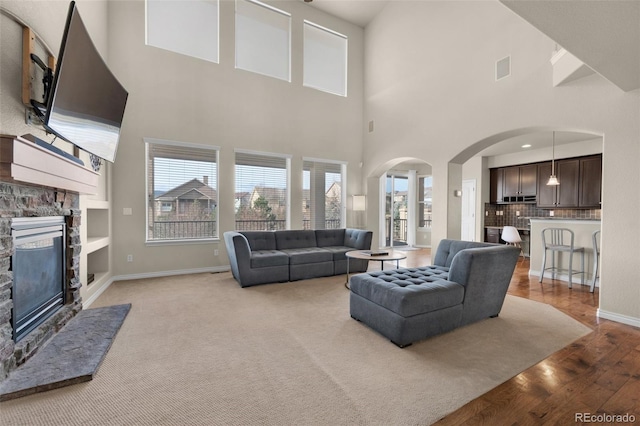 1053 Crystal Basin Dr, Colorado Springs, CO 80921 - living area featuring a stone fireplace, light wood finished floors, arched walkways, plenty of natural light, and a high ceiling