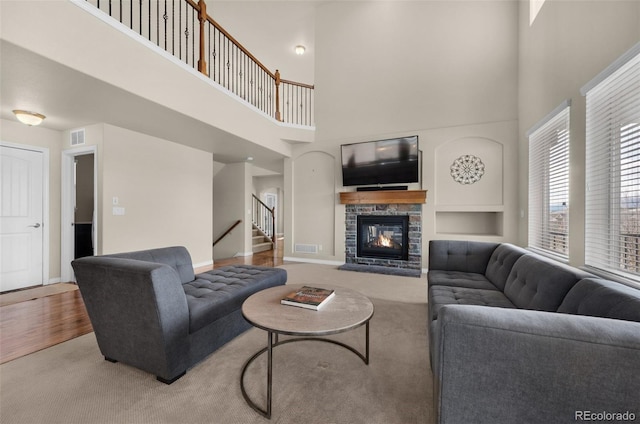 living room with wood-type flooring, a towering ceiling, and a stone fireplace