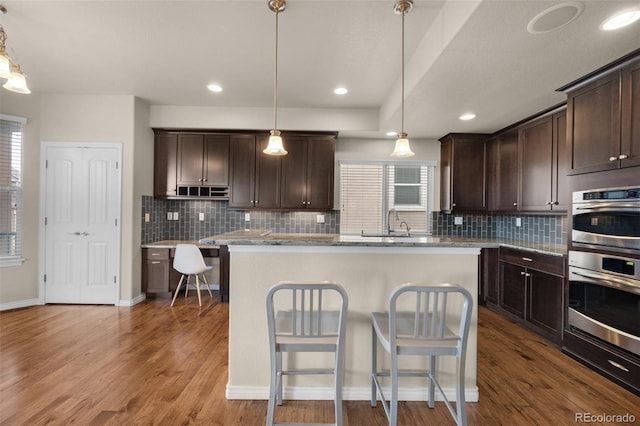 kitchen with light stone countertops, wood-type flooring, a kitchen island, and hanging light fixtures