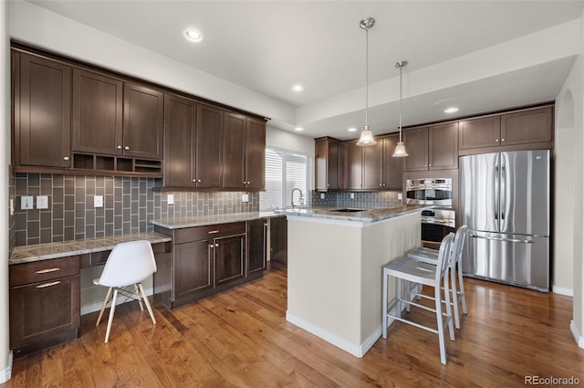 kitchen with light wood-type flooring, backsplash, stainless steel appliances, decorative light fixtures, and a kitchen island