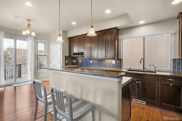 1053 Crystal Basin Dr, Colorado Springs, CO 80921 - kitchen featuring dark wood-style flooring, decorative backsplash, a kitchen breakfast bar, dark brown cabinetry, and a kitchen island