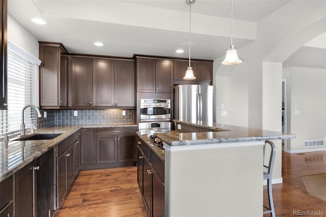 1053 Crystal Basin Dr, Colorado Springs, CO 80921 - kitchen featuring appliances with stainless steel finishes, wood finished floors, dark brown cabinets, a kitchen bar, and a center island