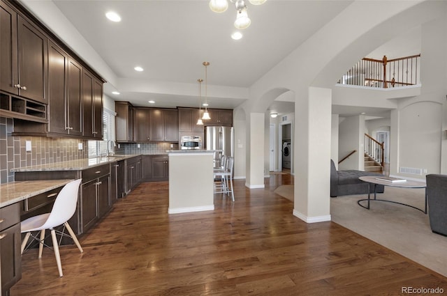 kitchen with appliances with stainless steel finishes, tasteful backsplash, dark wood-type flooring, a center island, and hanging light fixtures