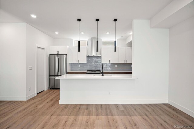 kitchen with white cabinetry, hanging light fixtures, stainless steel fridge, and light hardwood / wood-style flooring