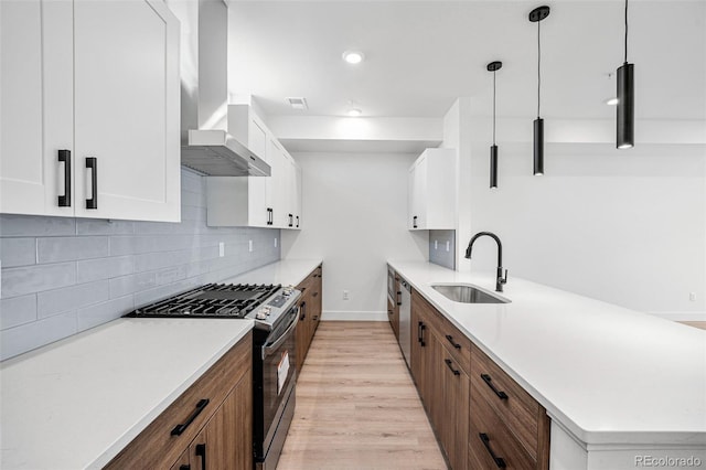 kitchen featuring wall chimney range hood, appliances with stainless steel finishes, sink, light hardwood / wood-style floors, and white cabinets