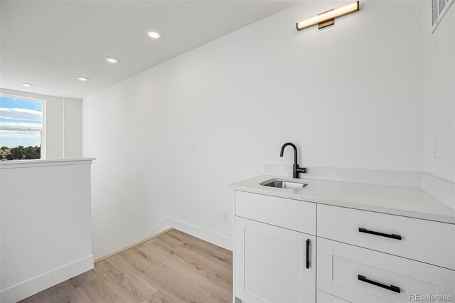 bar with light wood-type flooring, sink, and white cabinets