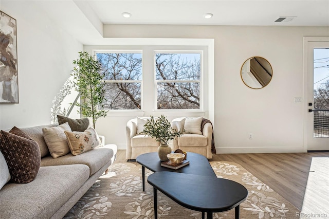 living room featuring a healthy amount of sunlight, visible vents, baseboards, and wood finished floors