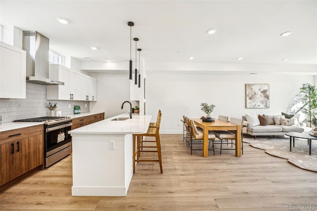 kitchen featuring a breakfast bar area, backsplash, stainless steel gas stove, a sink, and wall chimney range hood