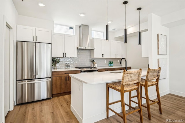 kitchen featuring stainless steel appliances, a sink, light wood-style floors, wall chimney range hood, and backsplash