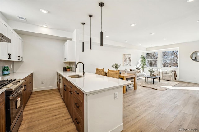 kitchen featuring visible vents, a peninsula, light wood-style floors, a sink, and gas stove