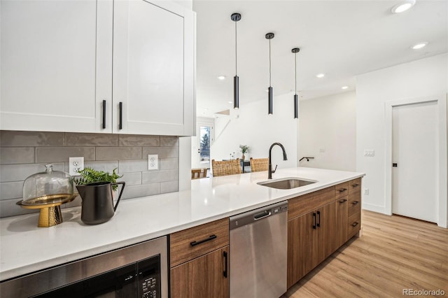 kitchen with light countertops, backsplash, stainless steel dishwasher, a sink, and light wood-type flooring