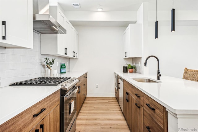 kitchen featuring visible vents, wall chimney exhaust hood, stainless steel appliances, light wood-style floors, and a sink