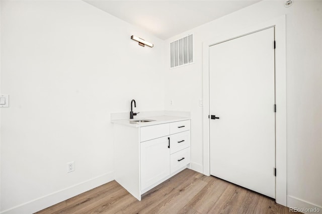 bathroom featuring visible vents, a sink, baseboards, and wood finished floors