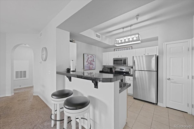 kitchen with white cabinetry, a breakfast bar area, light tile patterned floors, kitchen peninsula, and stainless steel appliances