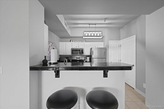 kitchen featuring a breakfast bar, appliances with stainless steel finishes, white cabinetry, light tile patterned flooring, and kitchen peninsula