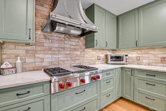 31112 Shadow Mountain Dr, Conifer, CO 80433 - kitchen with green cabinets, wall chimney exhaust hood, stainless steel gas stovetop, backsplash, and light stone counters