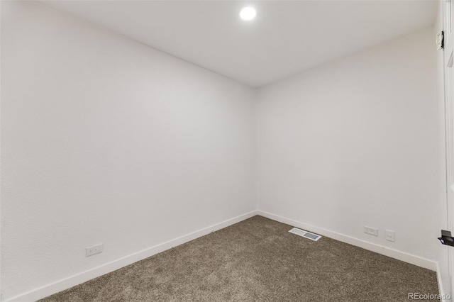 spare room with baseboards, visible vents, and dark carpet