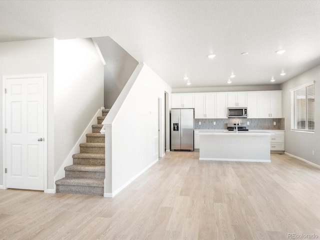 kitchen featuring appliances with stainless steel finishes, white cabinetry, an island with sink, backsplash, and light wood-type flooring