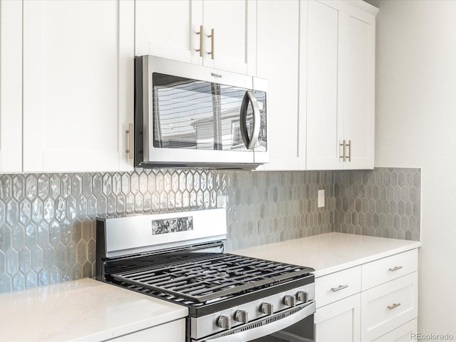 kitchen featuring stainless steel appliances, decorative backsplash, white cabinetry, and light stone countertops