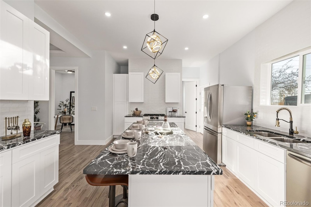 kitchen with sink, stainless steel appliances, a kitchen island, and dark stone countertops