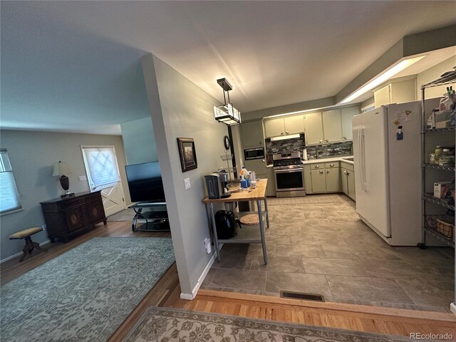 kitchen with stainless steel gas range oven, pendant lighting, backsplash, hardwood / wood-style flooring, and white refrigerator