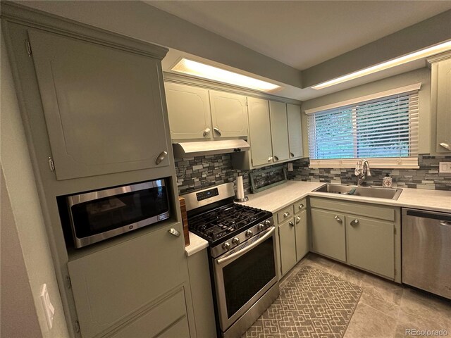 kitchen with gray cabinetry, light tile patterned floors, backsplash, appliances with stainless steel finishes, and sink