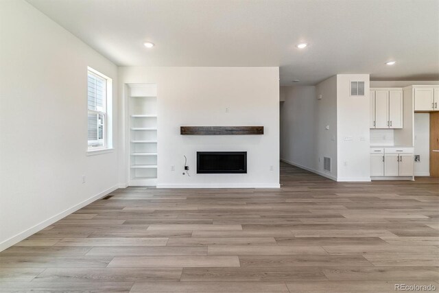 25254 E Warren Pl, Aurora, CO 80018 - unfurnished living room featuring a fireplace, baseboards, light wood finished floors, recessed lighting, and built in shelves