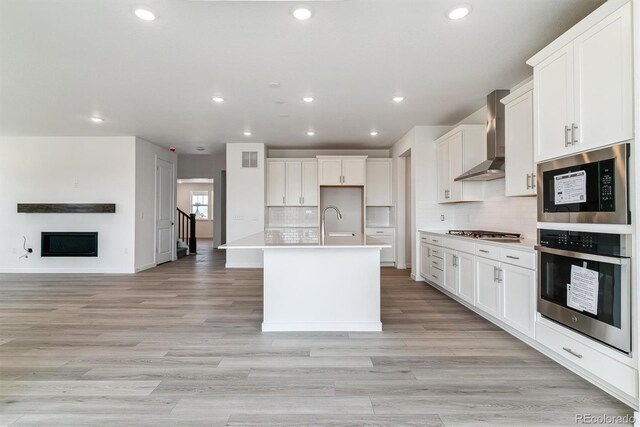 25254 E Warren Pl, Aurora, CO 80018 - kitchen featuring wall chimney exhaust hood, stainless steel appliances, open floor plan, recessed lighting, and a fireplace