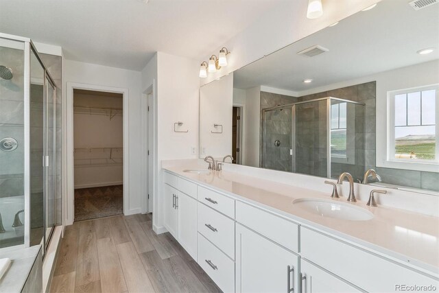 25254 E Warren Pl, Aurora, CO 80018 - bathroom featuring a walk in closet, a stall shower, double vanity, wood finished floors, and recessed lighting