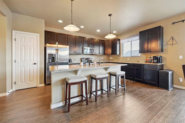 12766 Sunlight Peak Pl, Peyton, CO 80831 - kitchen with appliances with stainless steel finishes, dark wood-style floors, a center island with sink, recessed lighting, and a kitchen breakfast bar